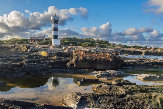 Black and white lighthouse on a rocky coast with vibrant sky and reflections in water.