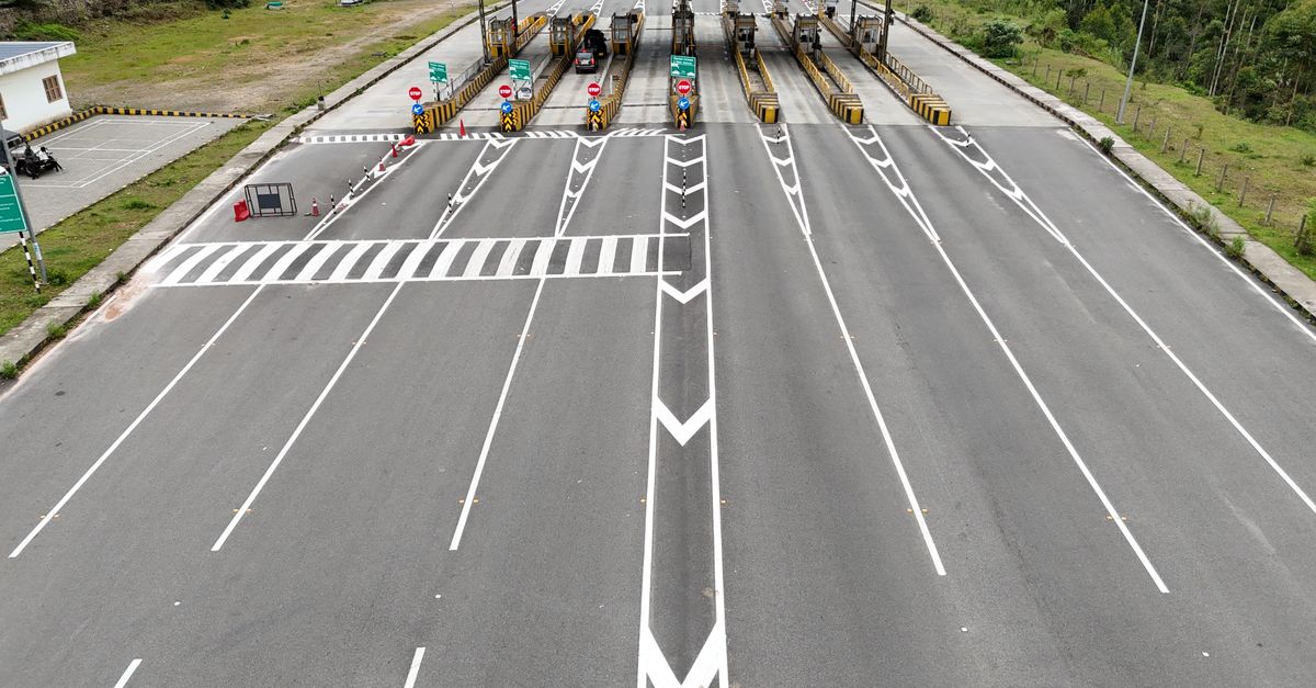 Aerial shot of an empty multi-lane toll booth on a highway surrounded by greenery.