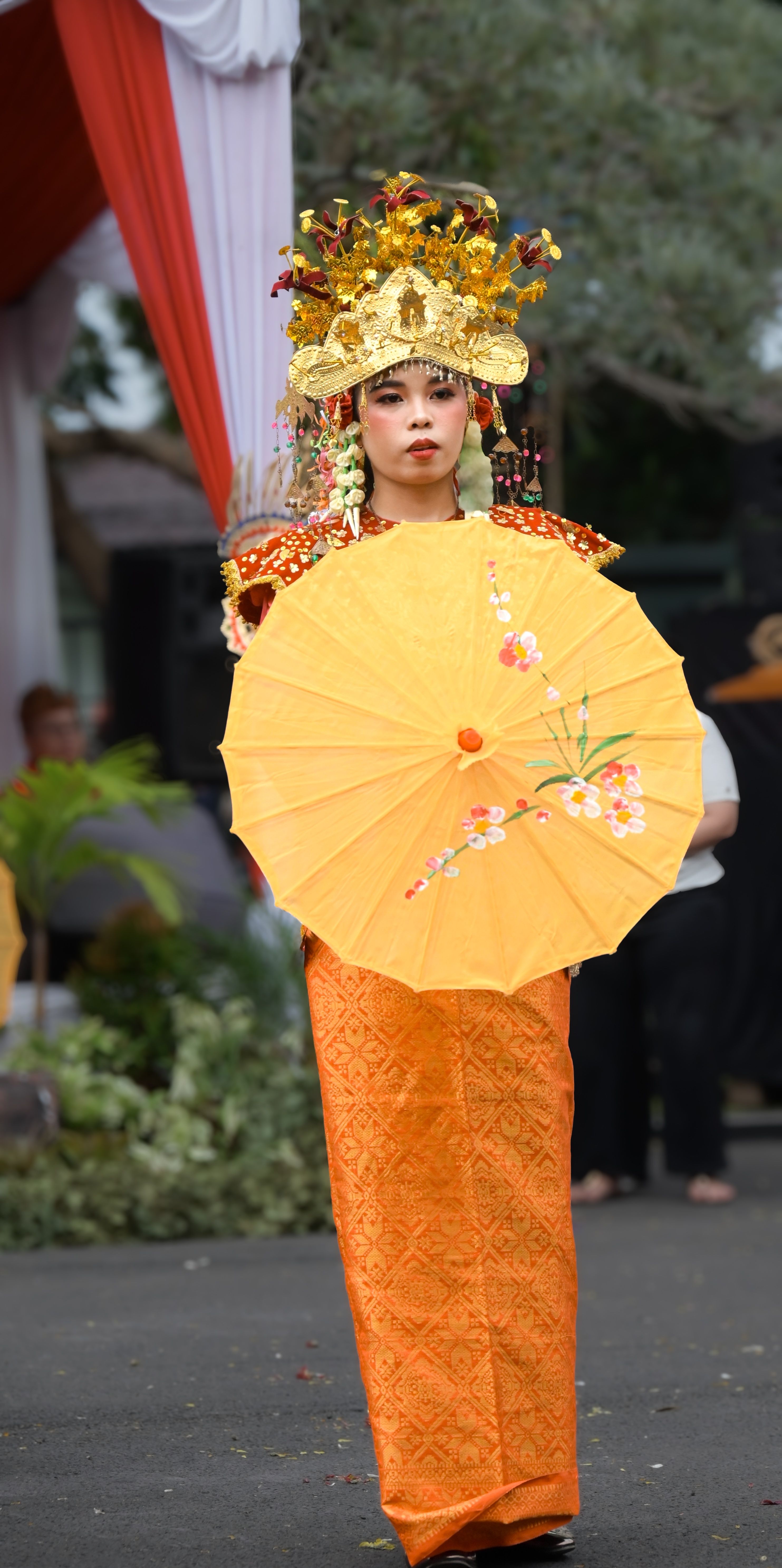 A person in vibrant traditional attire holds a decorative umbrella during a cultural parade.