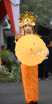 A person in vibrant traditional attire holds a decorative umbrella during a cultural parade. - Fotografer Sidoarjo