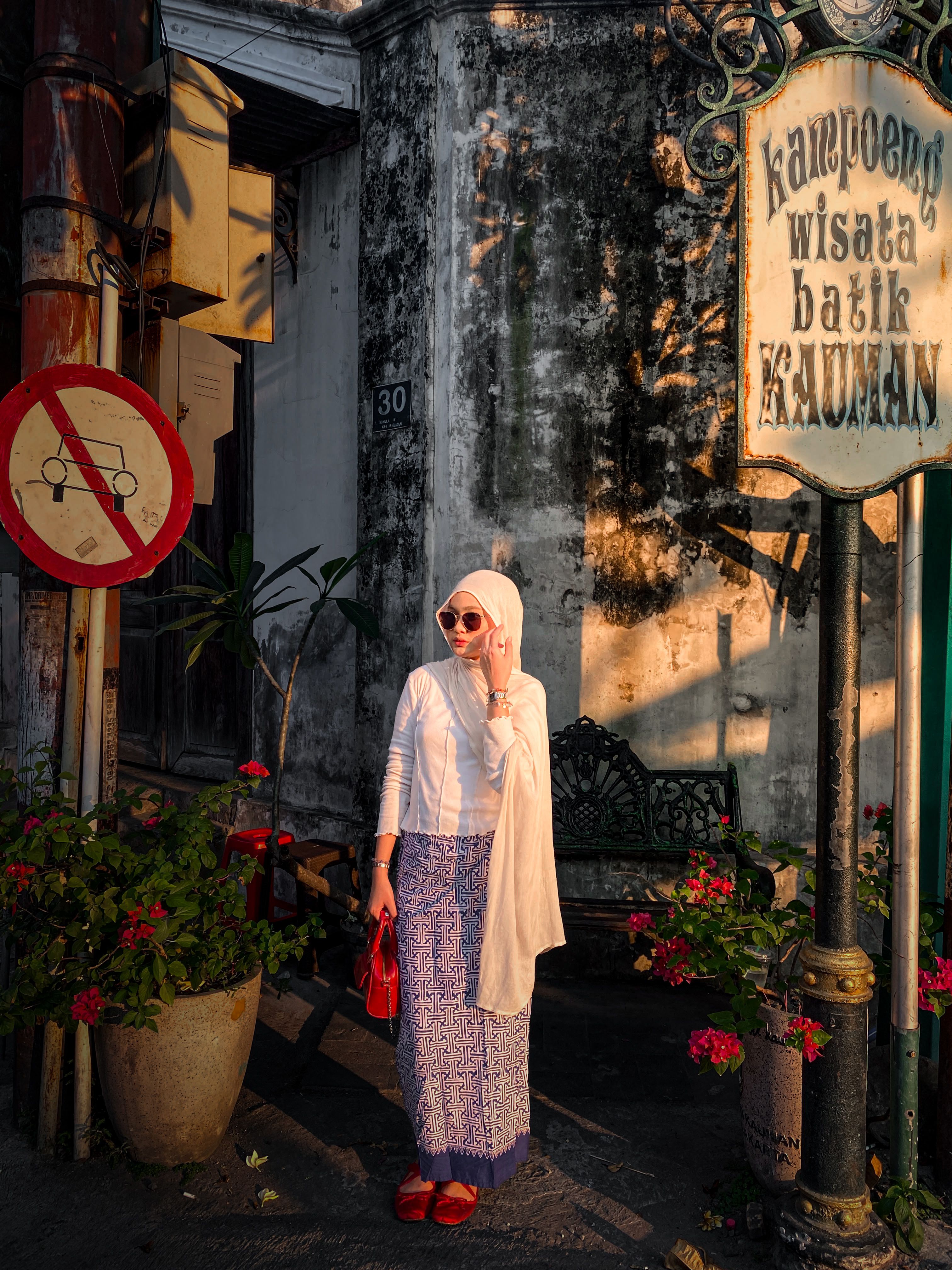 A woman in traditional batik stands in front of Kauman Batik Village sign in Jawa Tengah, Indonesia.