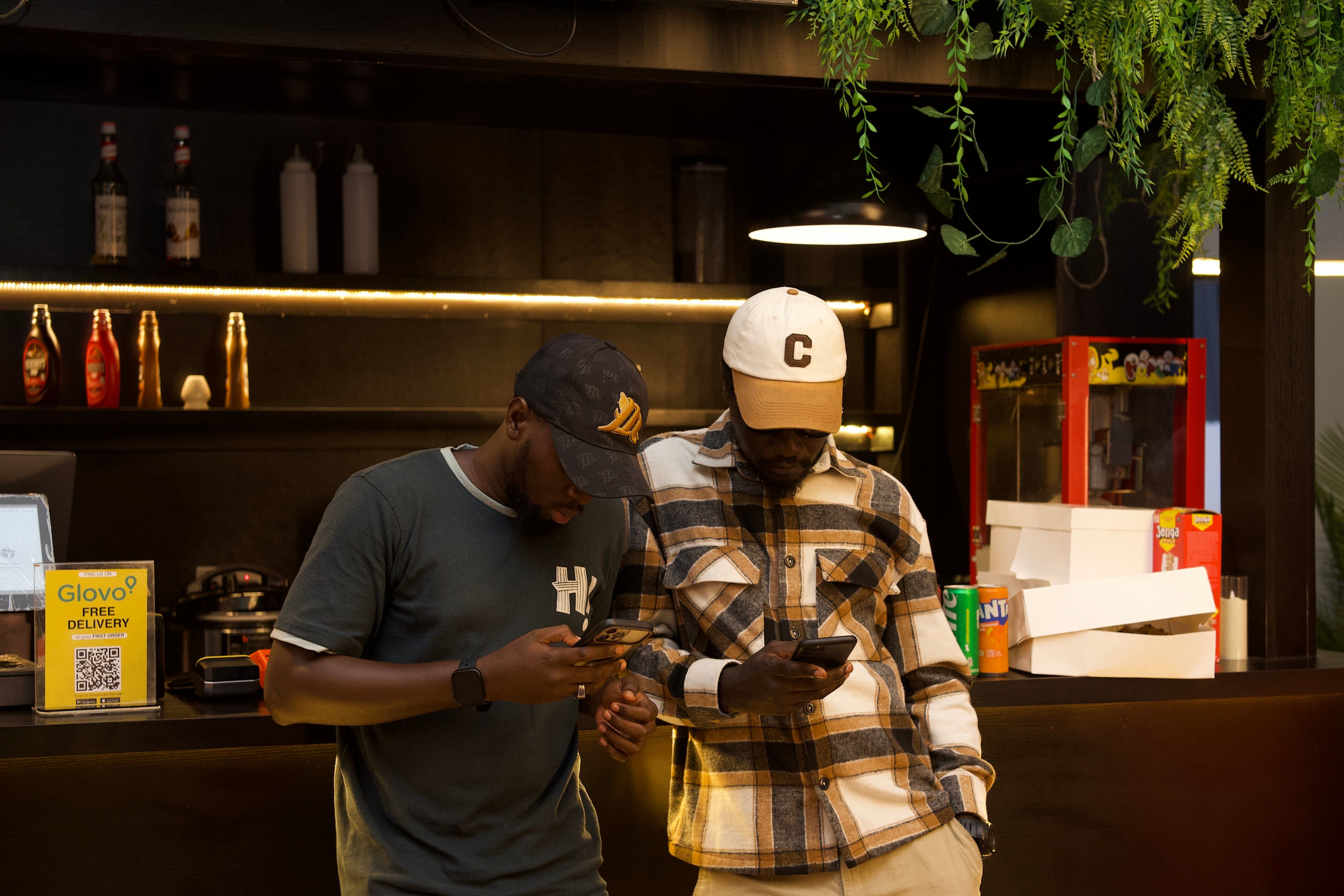 Two men in a stylish, modern indoor setting, focused on their smartphones.