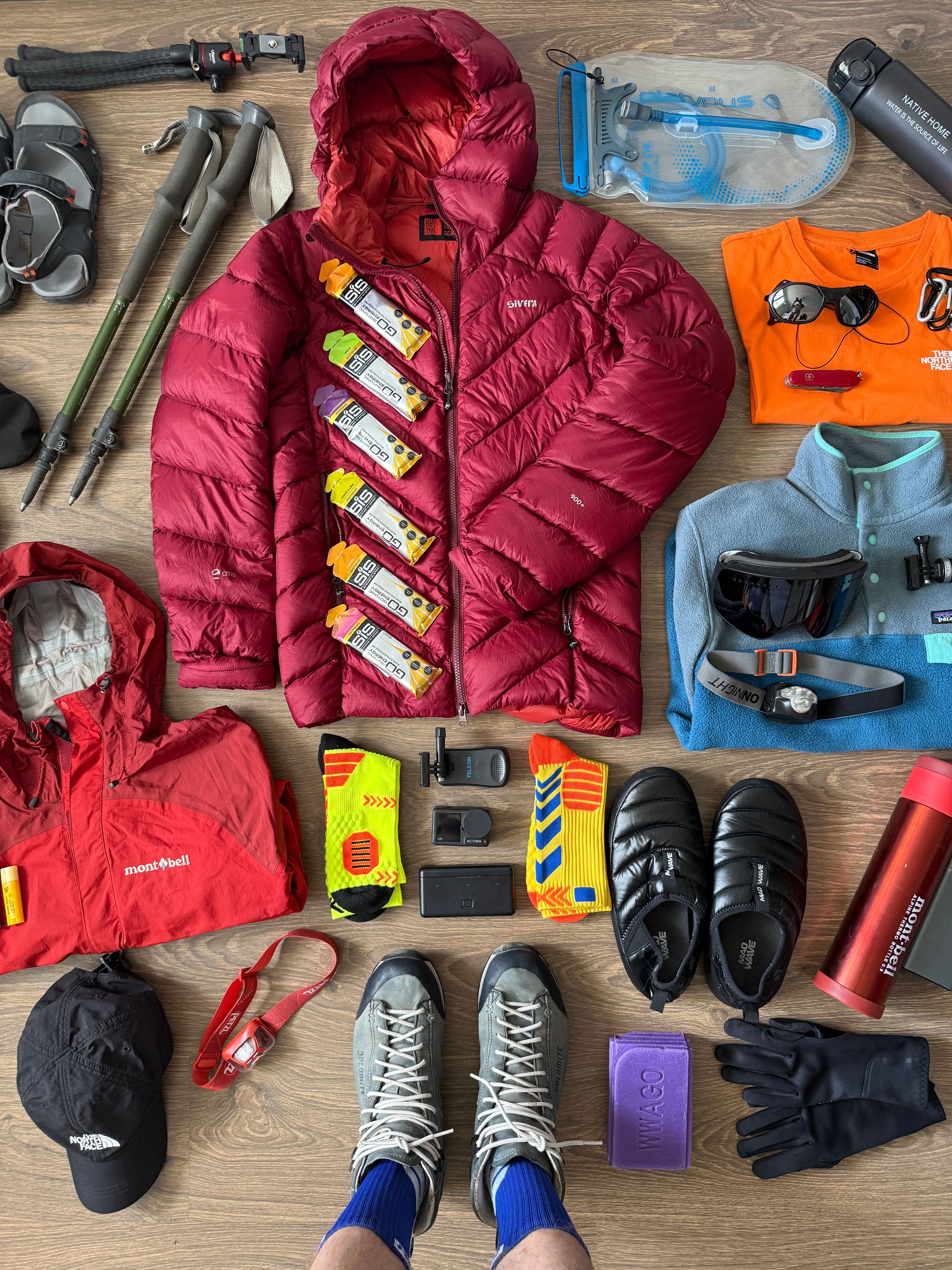 Camping gear laid out on a tarp with rain jacket, extra layers, and tent stakes ready for changing weather