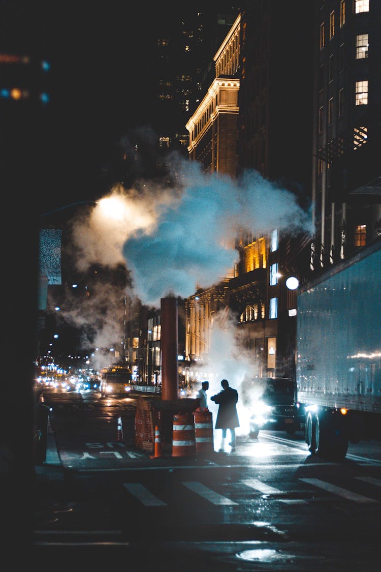 Unrecognizable Men Interacting On Night City Street Under Smoke Cloud