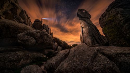 Free A lone explorer with a headlamp shines light in a rocky, starry landscape. Stock Photo