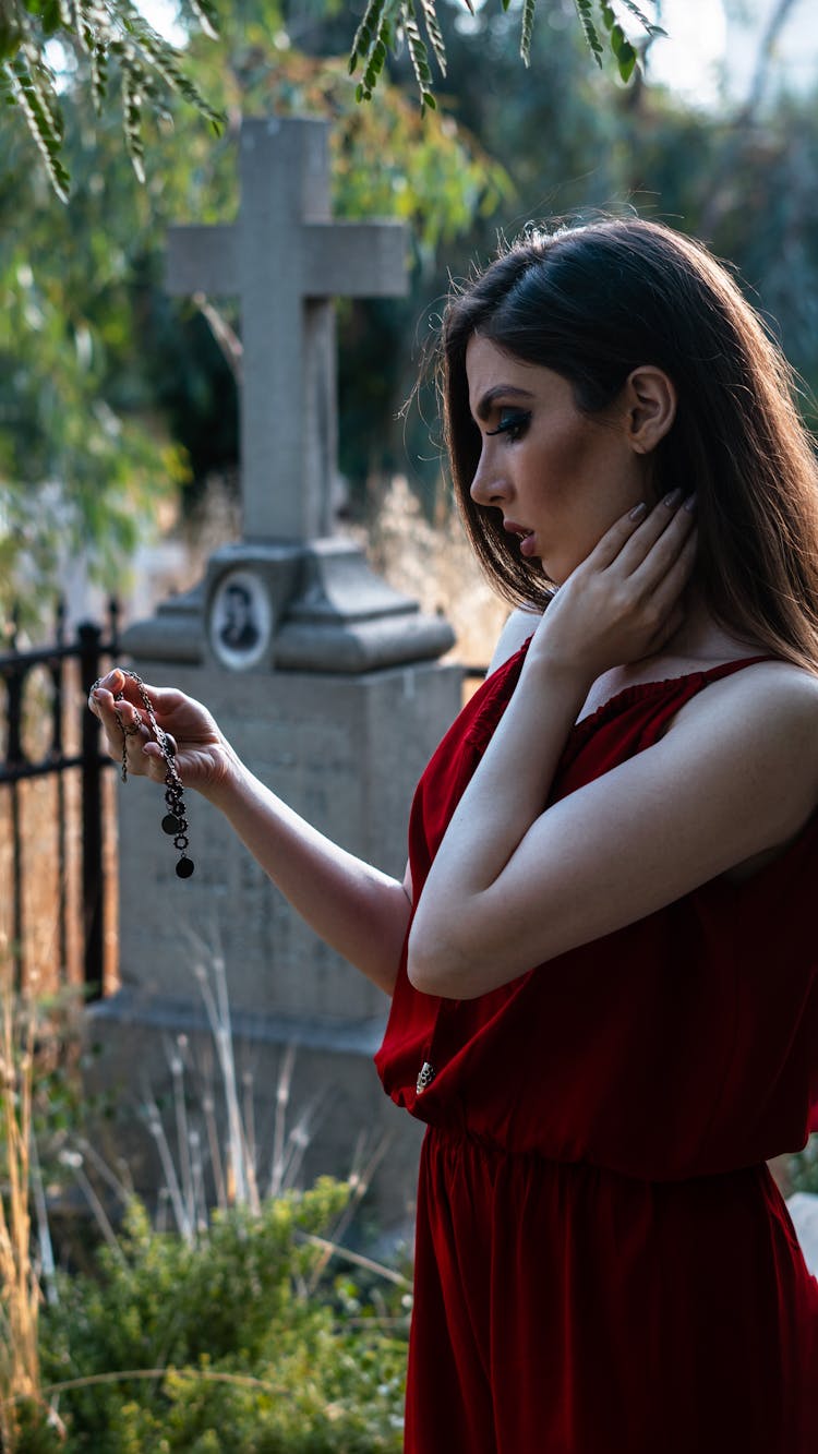 Thoughtful Lady Standing With Wristband Near Stone Grave With Cross