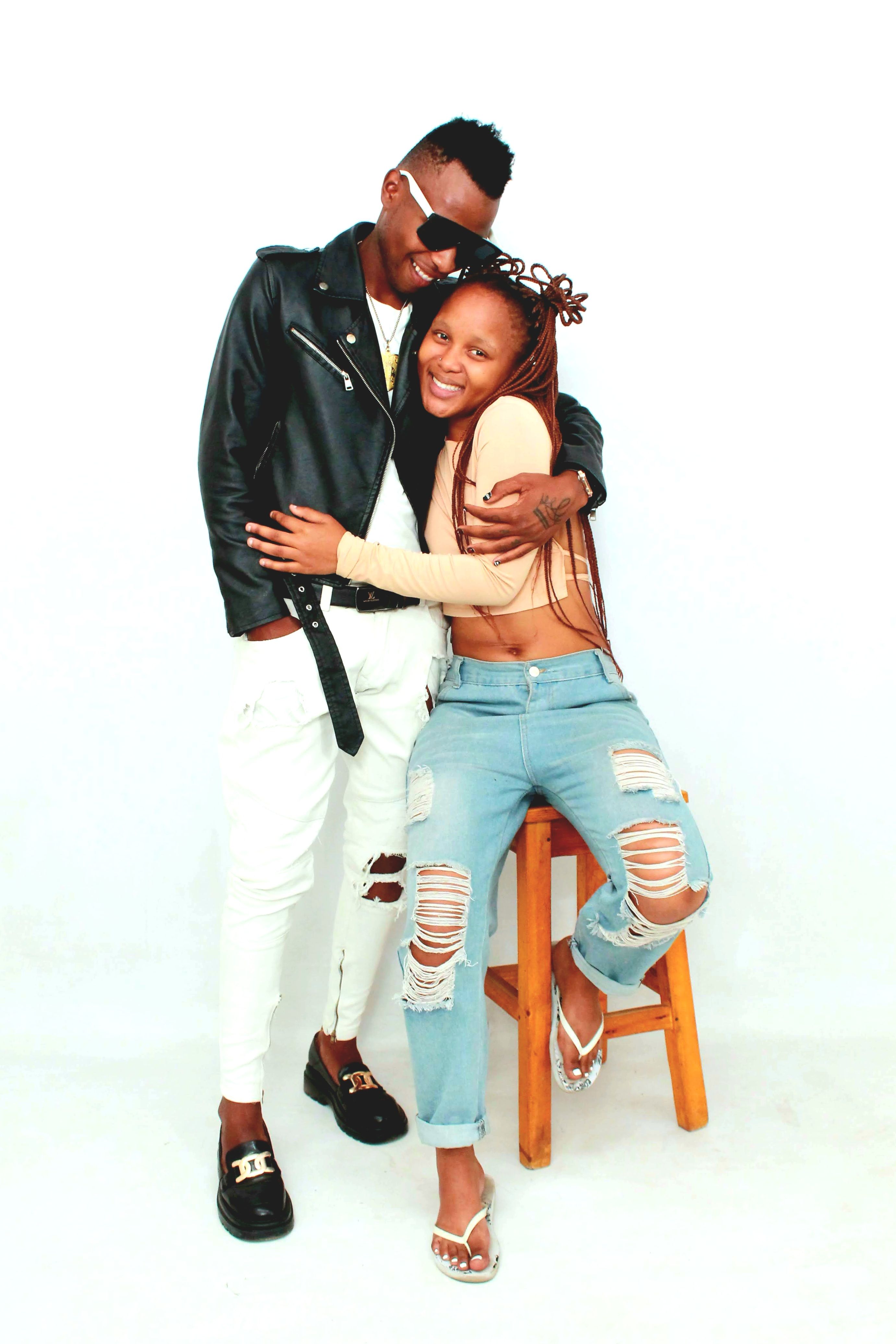 A cheerful young couple in casual and stylish outfits embraces indoors, exuding happiness.
