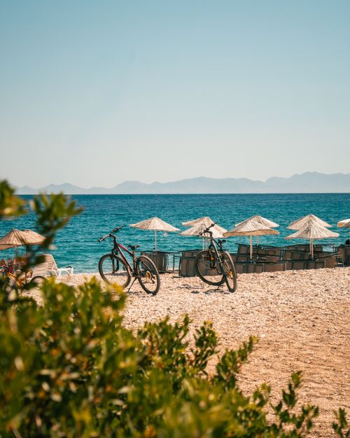 Free A serene beach scene with bicycles, parasols, and the ocean under a clear sky. Stock Photo
