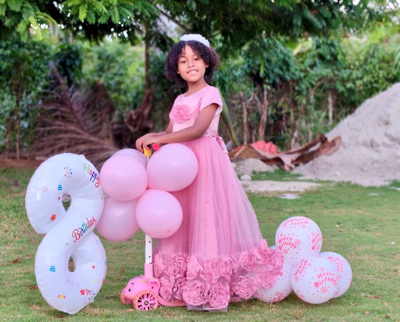 Fotomural Una niña pequeña con un vestido rosa celebra su cumpleaños con globos al aire libre.