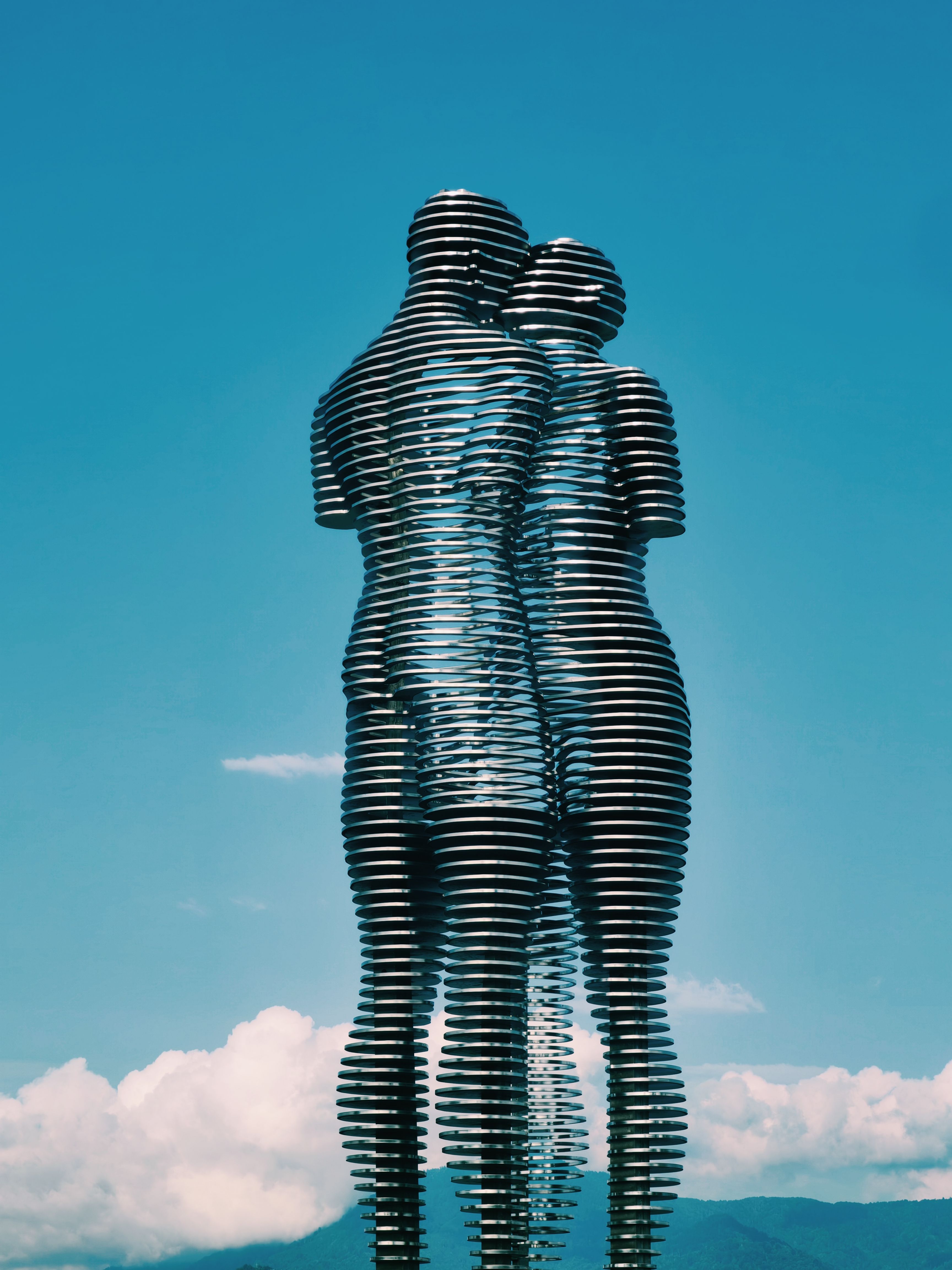 Dynamic metal sculpture of embracing figures against a blue sky.