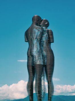 Dynamic metal sculpture of embracing figures against a blue sky.