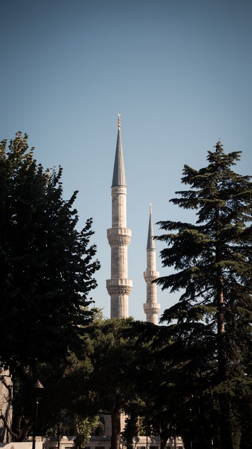 Free Captivating landscape featuring mosque minarets framed by trees under a clear sky. Stock Photo