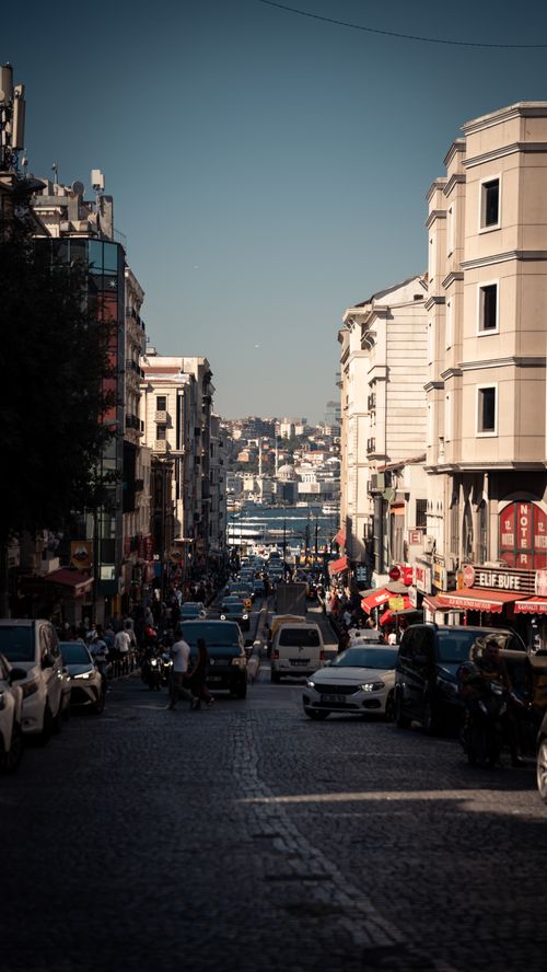 Free Vibrant city street scene with cars and pedestrians leading to a distant sea view. Stock Photo