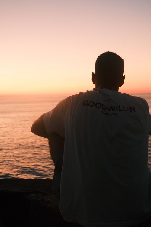 Free A person sitting by the ocean at sunset, enjoying the serene view. Stock Photo