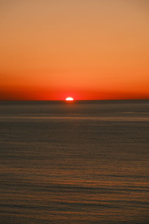 Free Capture of a vibrant orange sunset over the calm sea, creating a serene atmosphere. Stock Photo