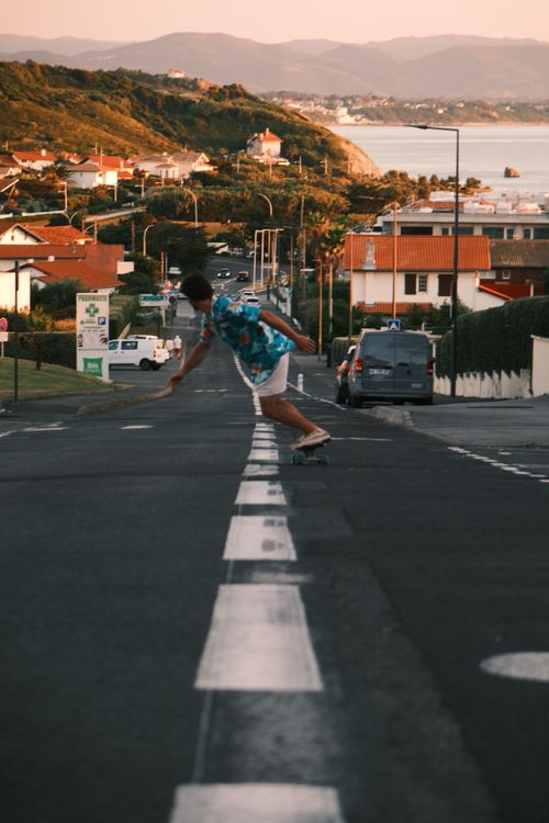 Free A teenager skateboards down a scenic coastal road during a beautiful sunset, capturing a sense of freedom. Stock Photo