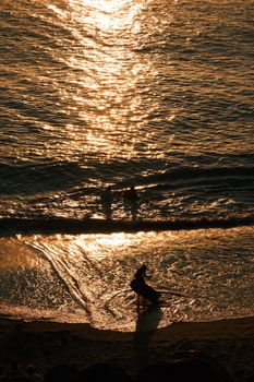 Silhouetted person walking on the beach during a golden sunset. Calm and serene ocean scene.