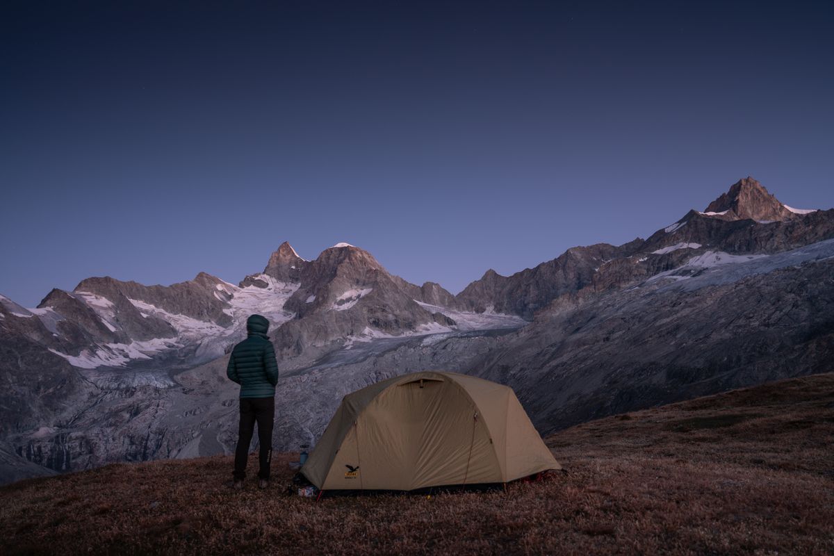Camper beside a tent below snowy alpine peaks