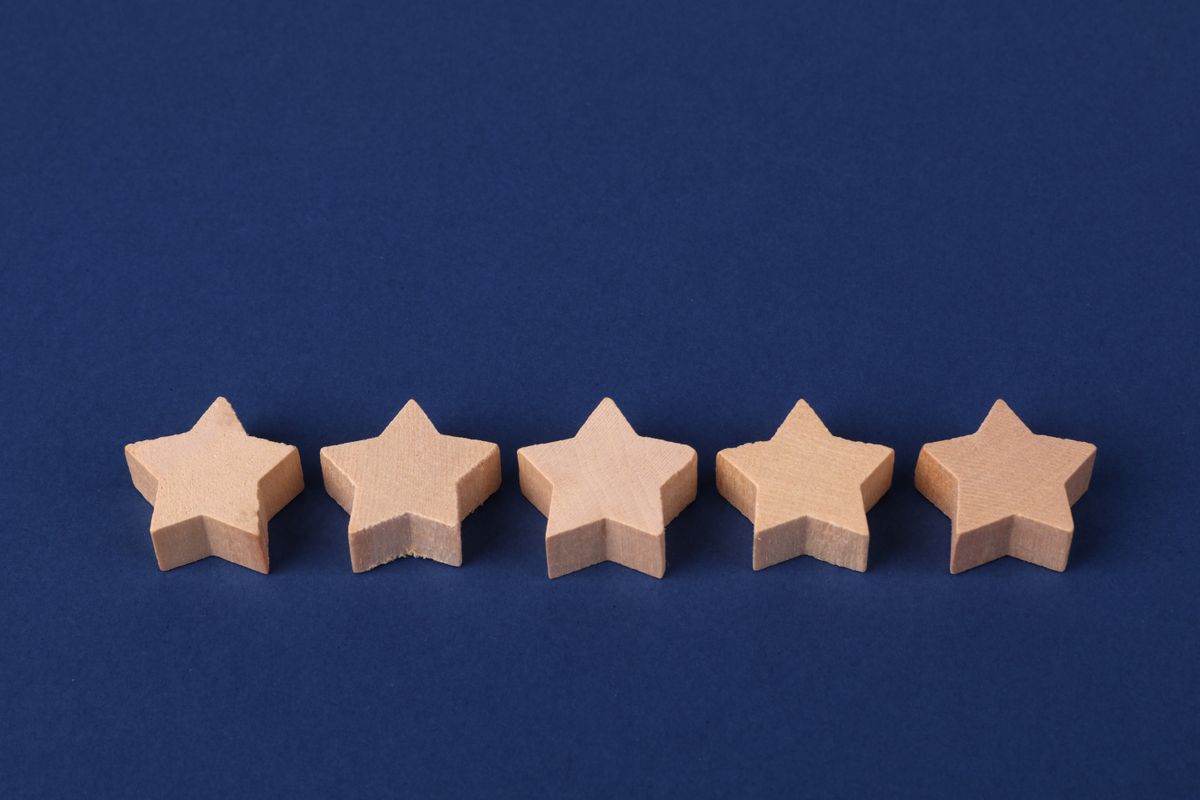 Five wooden star shapes in a row on a dark blue background, representing a review rating