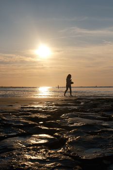 A silhouette of a woman walking along the beach during sunset, creating a serene and calming atmosphere.
