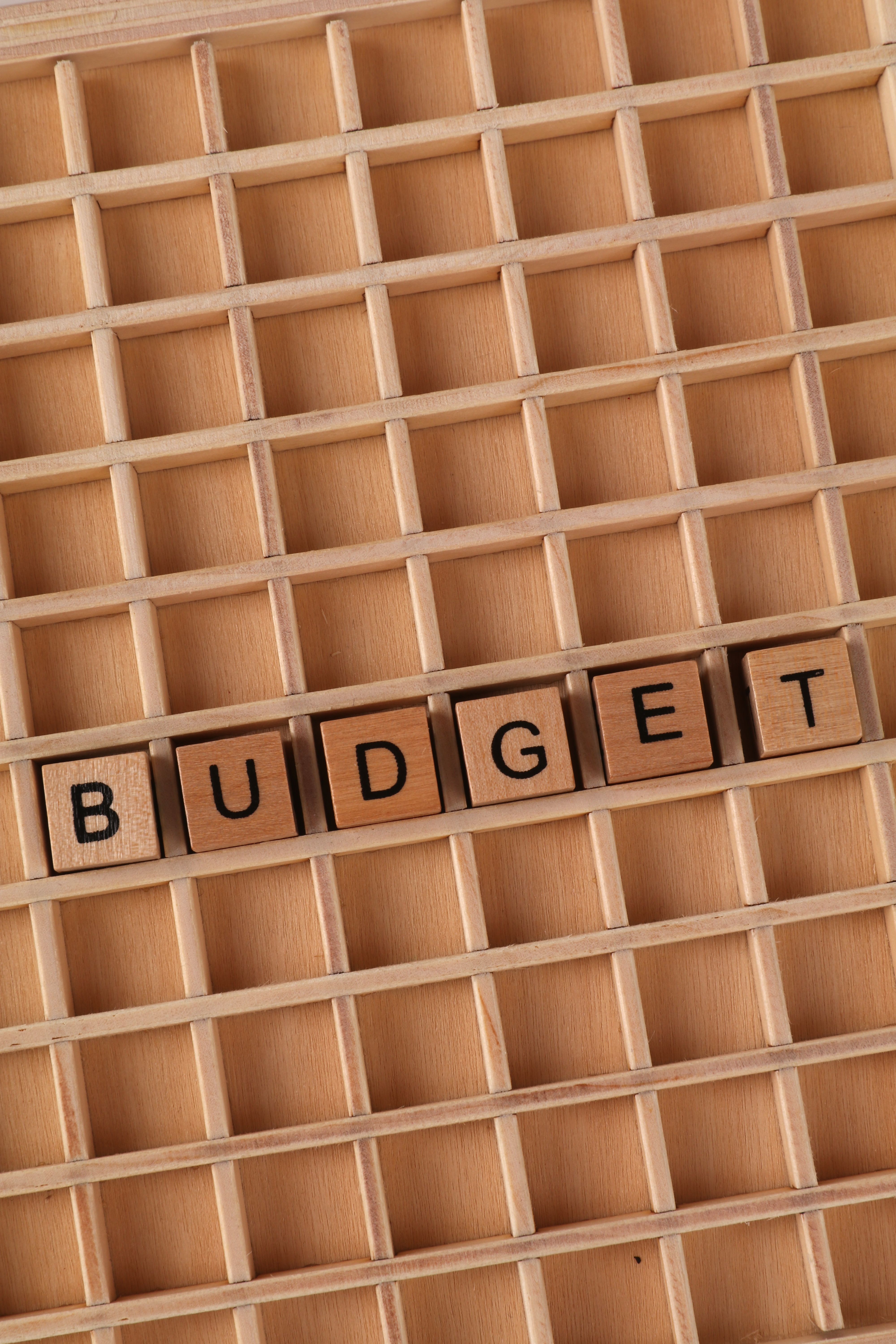 Wooden blocks arranged to spell 'Budget' on a lattice background, emphasizing financial planning.