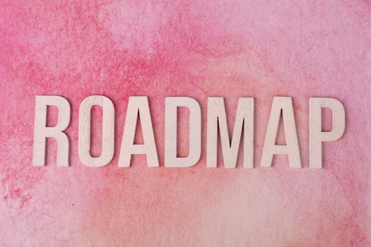 Wooden letters spelling 'ROADMAP' on a vibrant pink watercolor background.