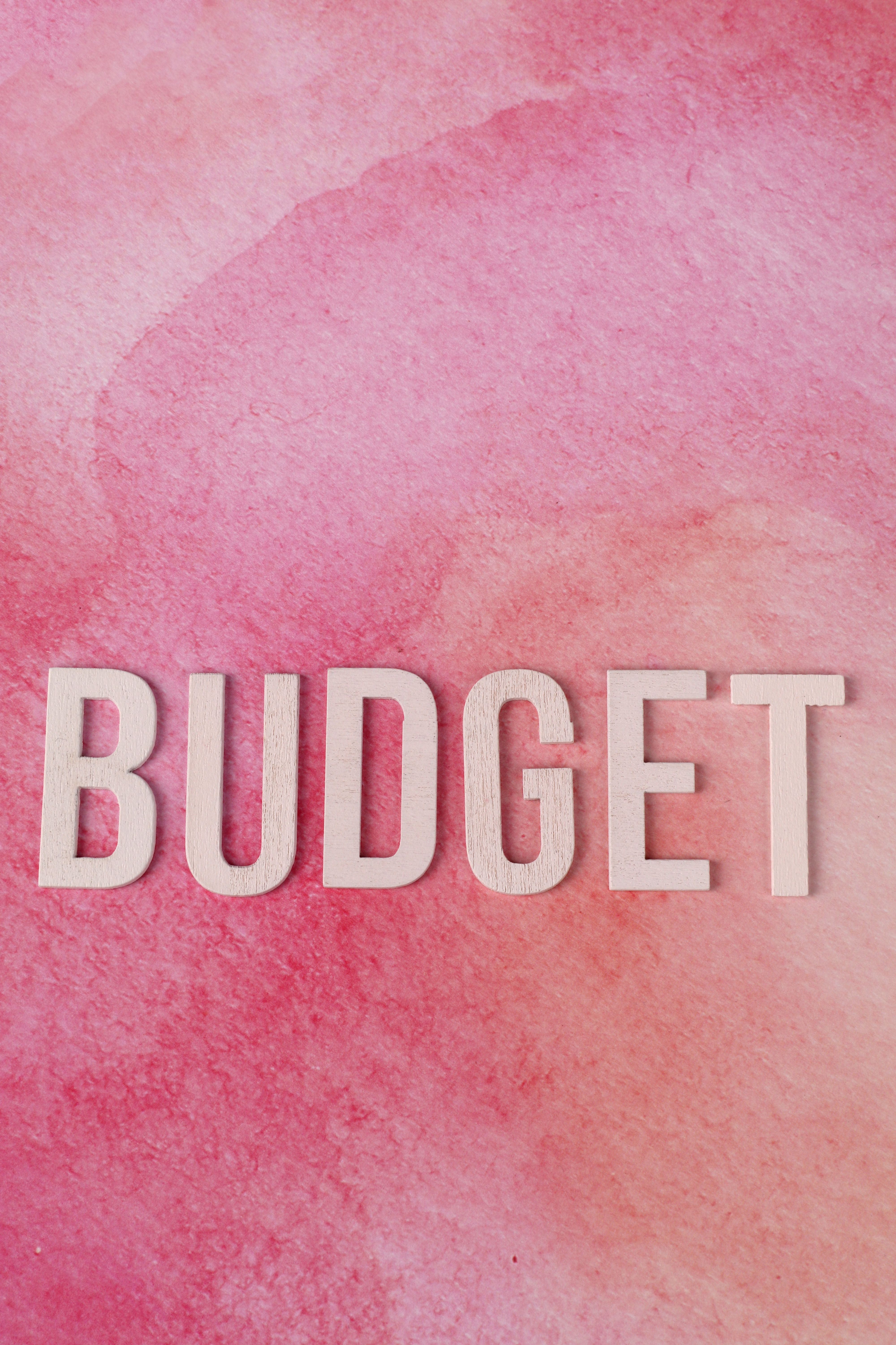 White letters spelling 'BUDGET' on a pink watercolor background signify financial planning.