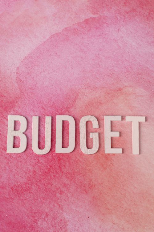 Free White letters spelling 'BUDGET' on a pink watercolor background signify financial planning. Stock Photo