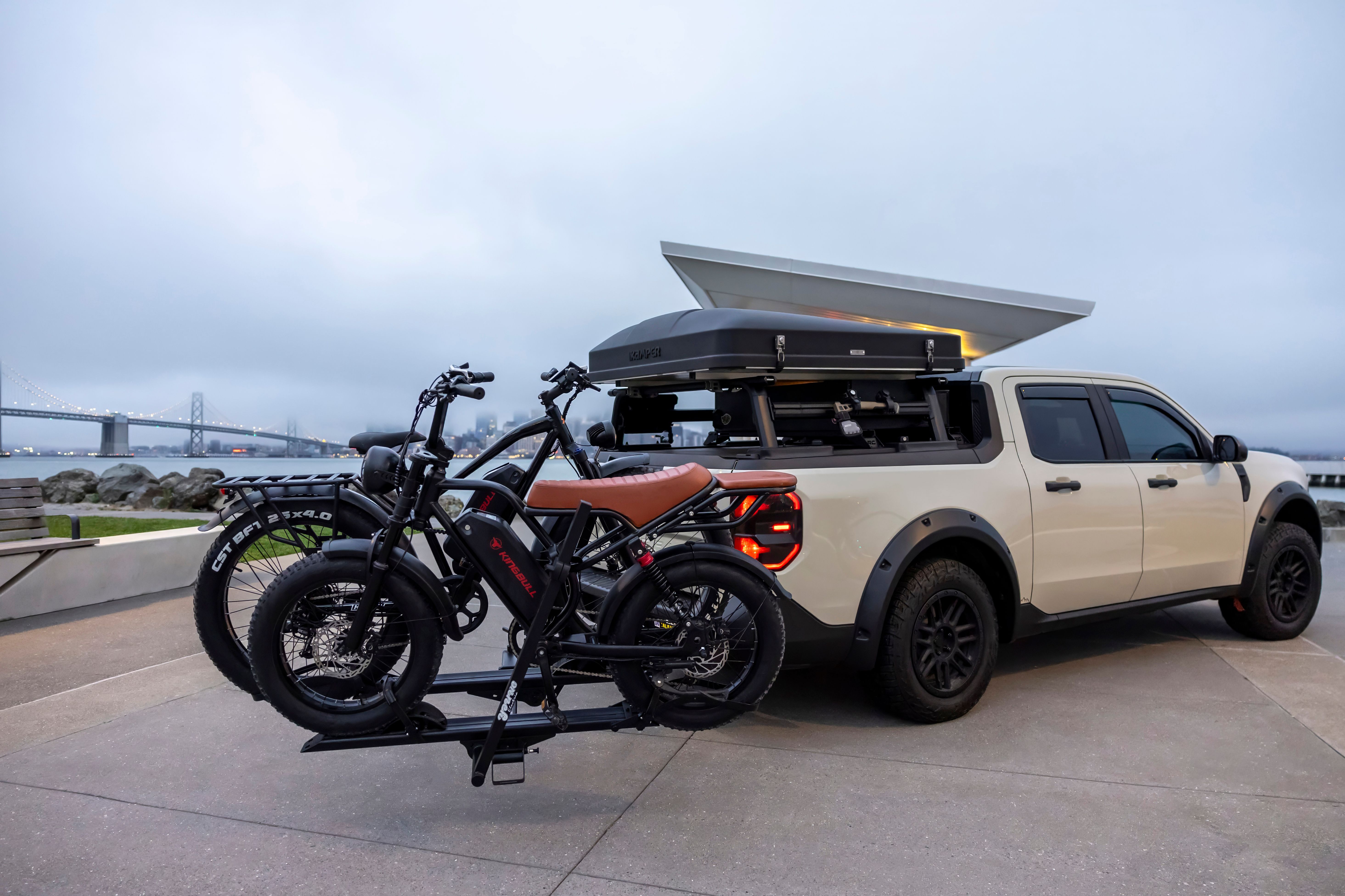 Adventure truck carrying e-bikes parked near the Bay Bridge on a cloudy day.