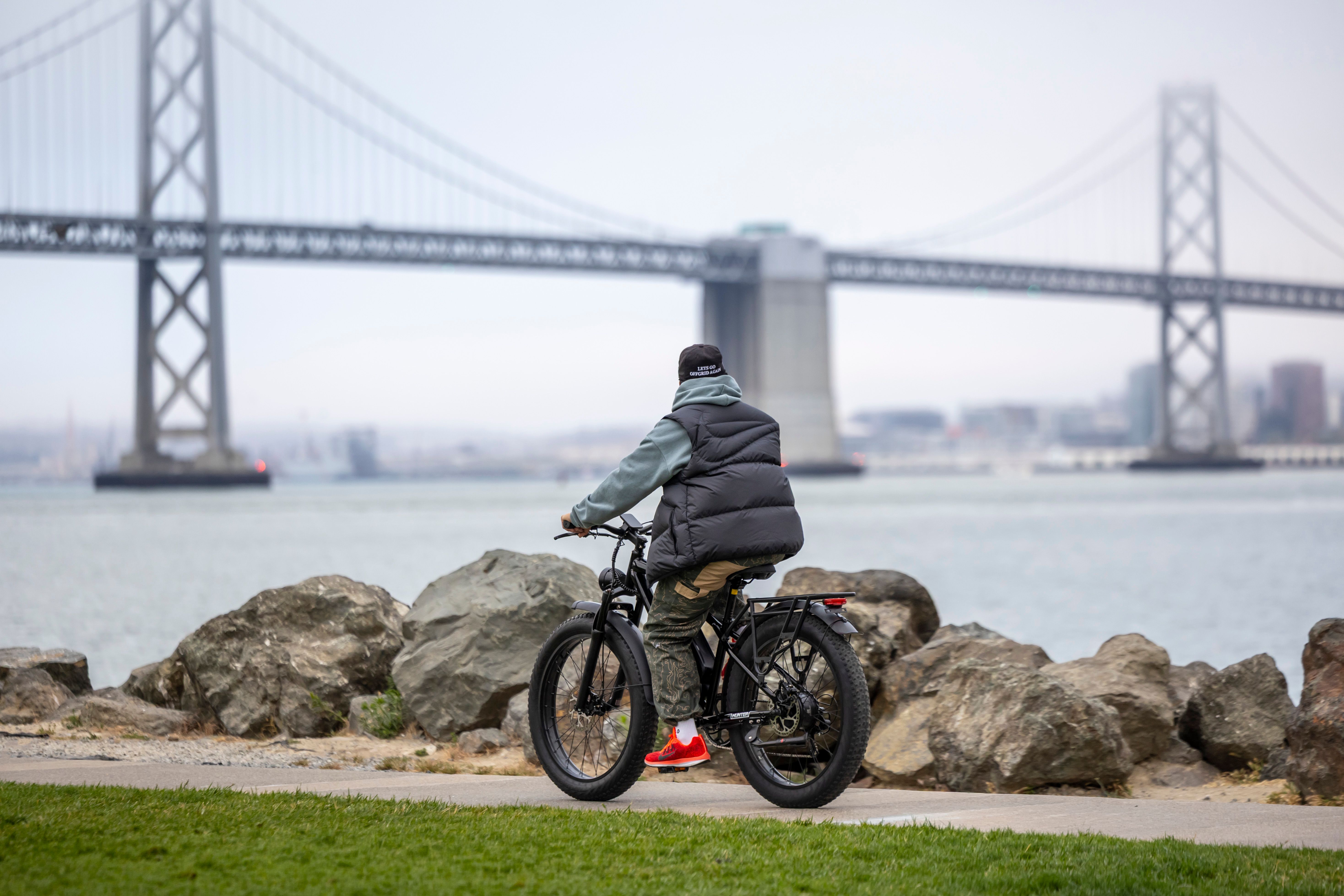 Cyclist riding an electric bike past the Bay Bridge in San Francisco.