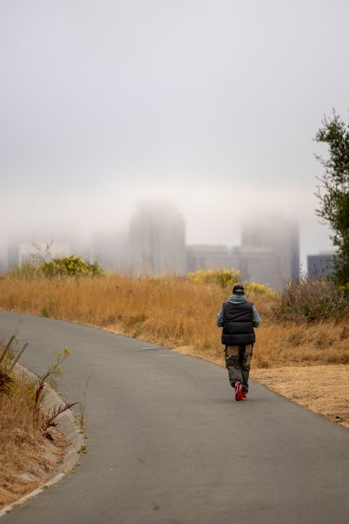 Free A person walks along a foggy path with a blurred city skyline in the background, creating a moody atmosphere. Stock Photo