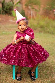 A young girl in a vibrant dress with a party hat enjoys her outdoor birthday celebration.