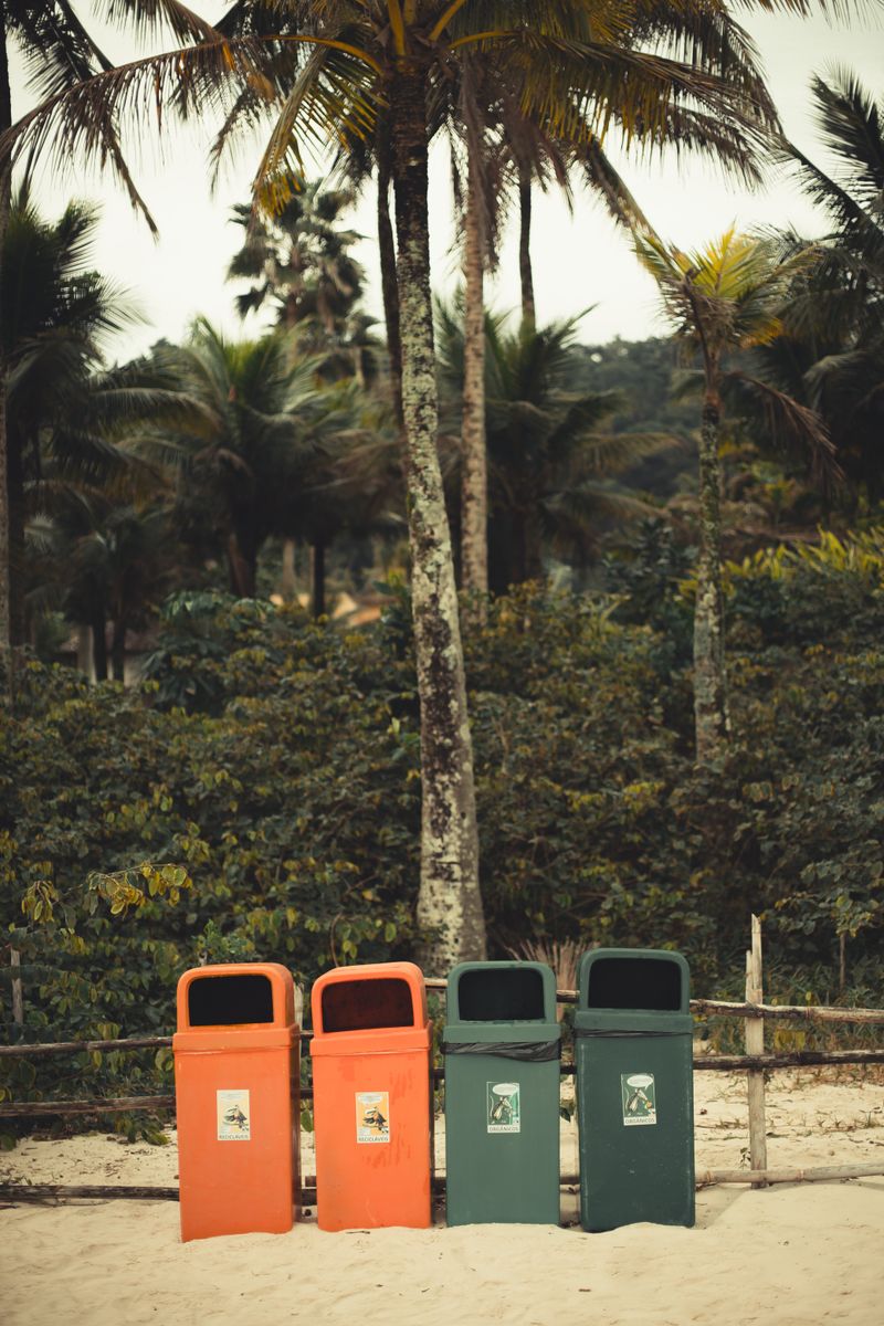 Tropical beach scene with colorful recycling bins amid palm trees, promoting eco-friendliness.