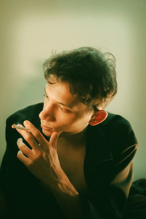 Free A young man in low light holds a cigarette, lost in thought. Artistic and moody portrait. Stock Photo