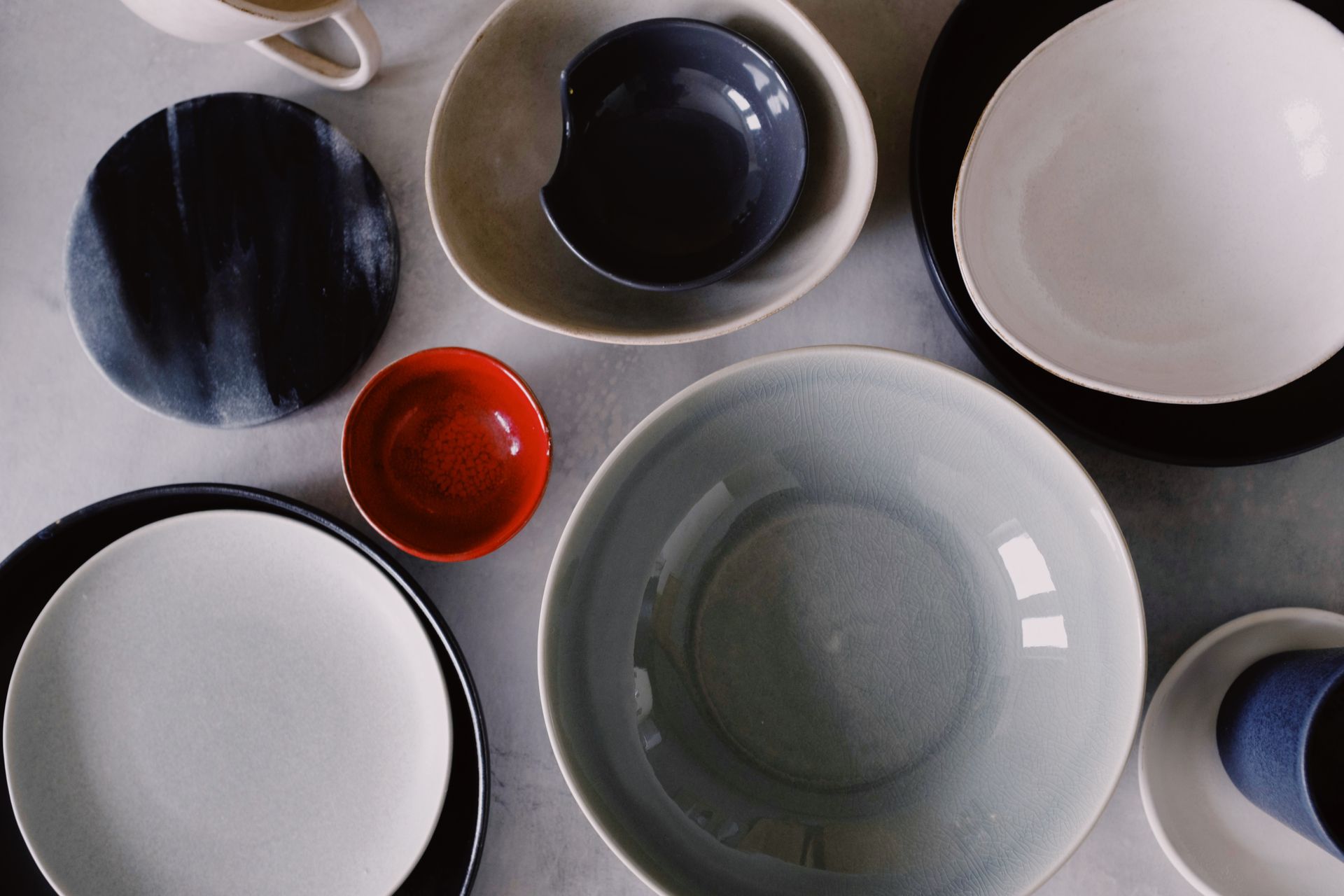 Overhead flat-lay of colorful ceramic plates and bowls in blue, black, red and white glazes on a light surface