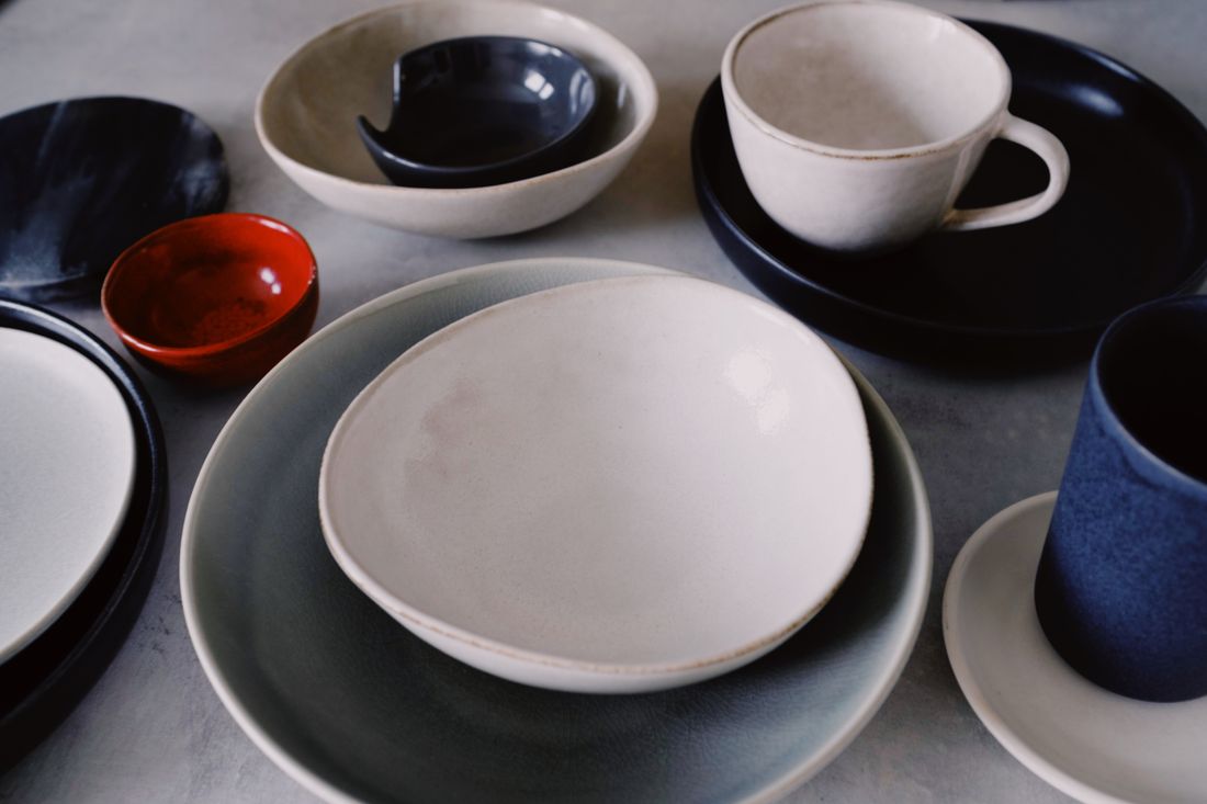 Bowls, cups and plates in several glazes set out on a table