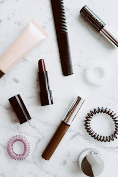 A stylish assortment of beauty products including lipstick, comb, and elastics on a marble surface.