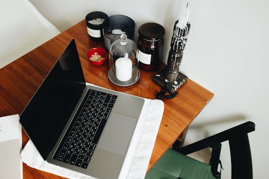 A home office with a laptop on a wooden table, surrounded by candles and jars for a warm atmosphere.
