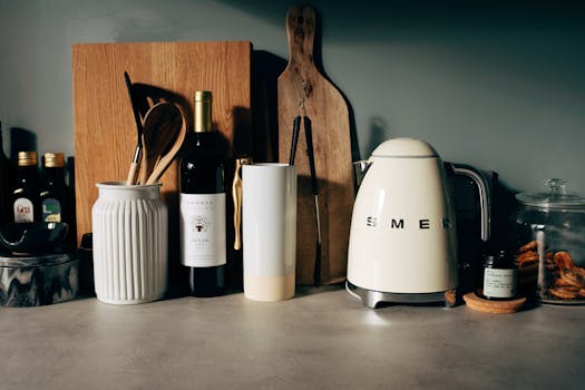 White gloss electric kettle standing next to other kitchen utensils with bottle of wine and various bowls on countertop in modern home kitchen