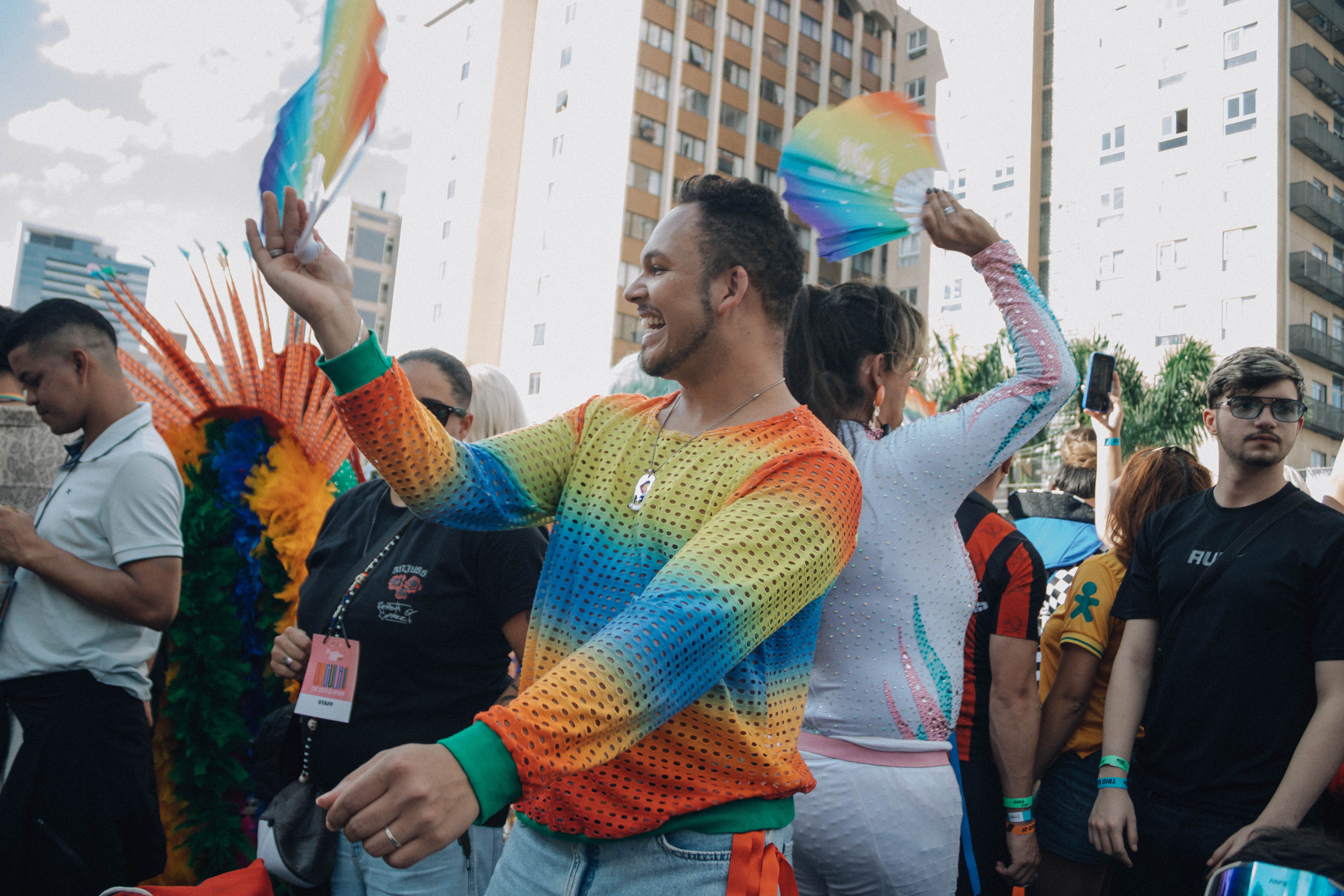 Colorful crowd celebrating at an outdoor pride parade with rainbow flags and festive outfits.