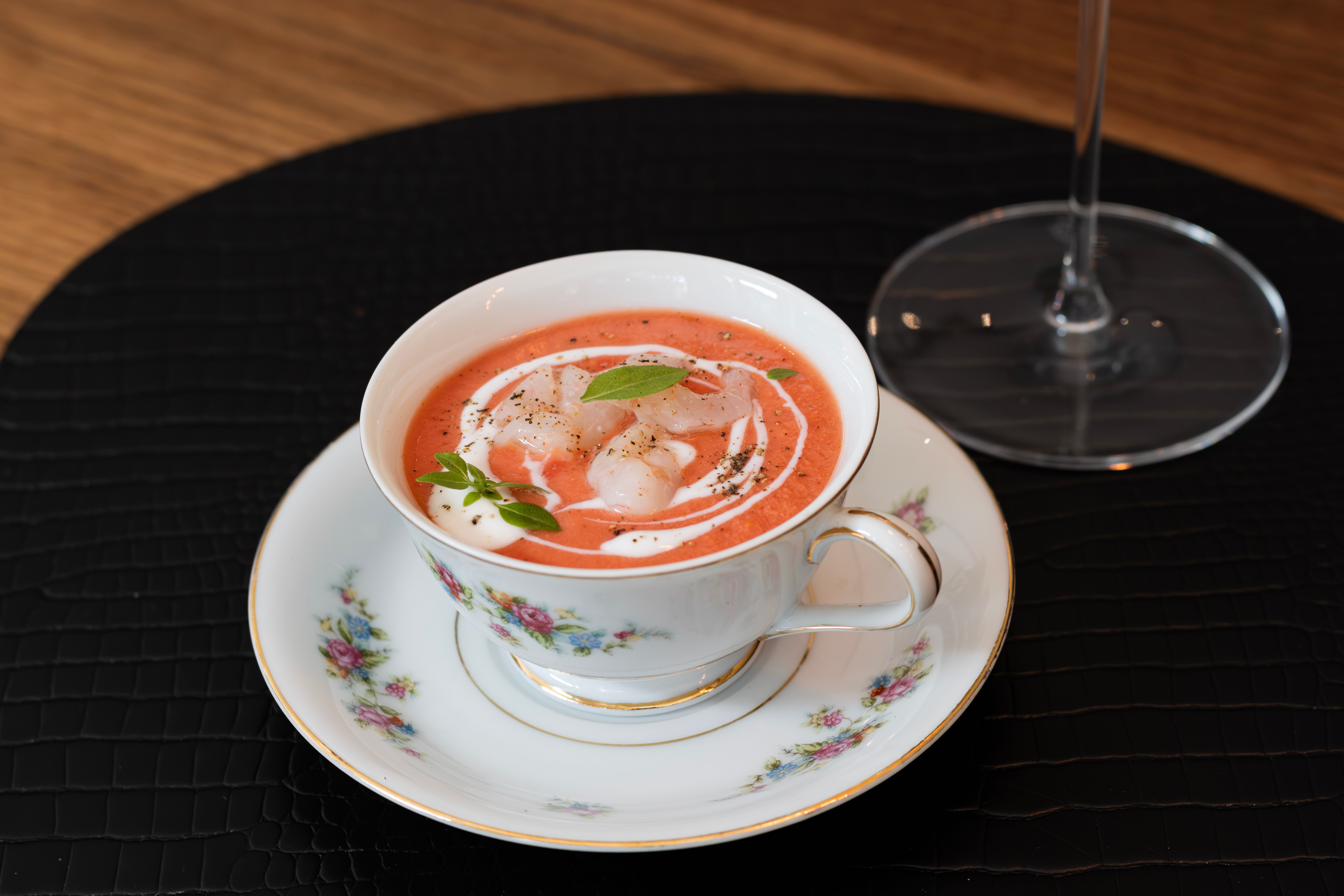 A white bowl of creamy orange-red tomato bisque with a swirl of cream on top, fresh basil leaves, and croutons scattered around the bowl.