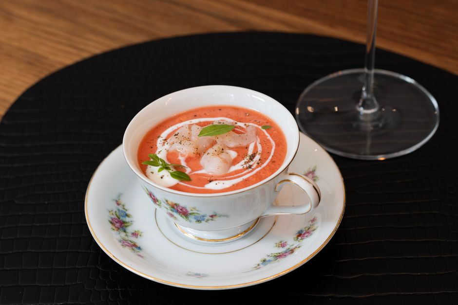 A white bowl of creamy orange-red tomato bisque with a swirl of cream on top, fresh basil leaves, and croutons scattered around the bowl.
