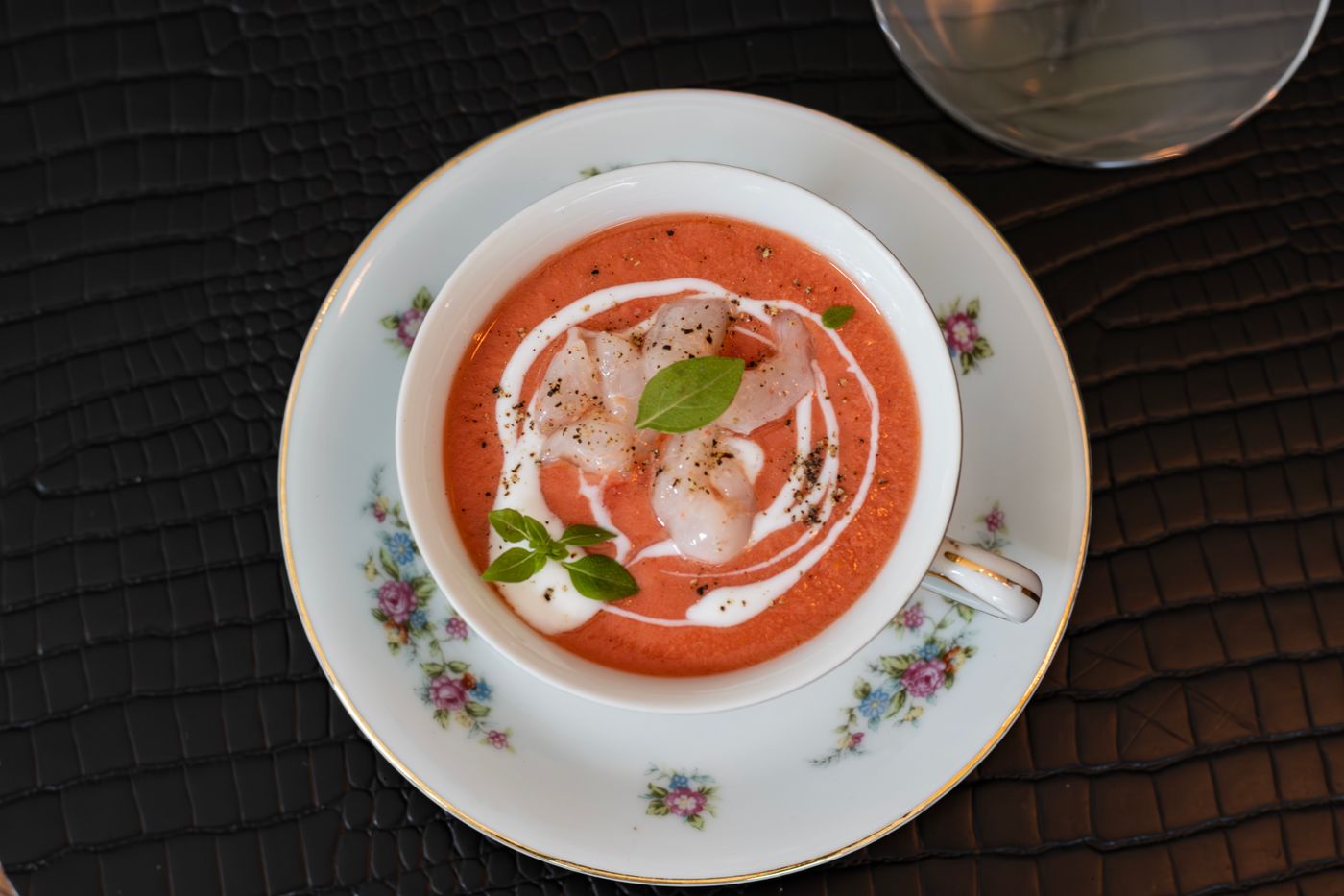 Stylish tomato gazpacho served in a floral tea cup with basil garnish.