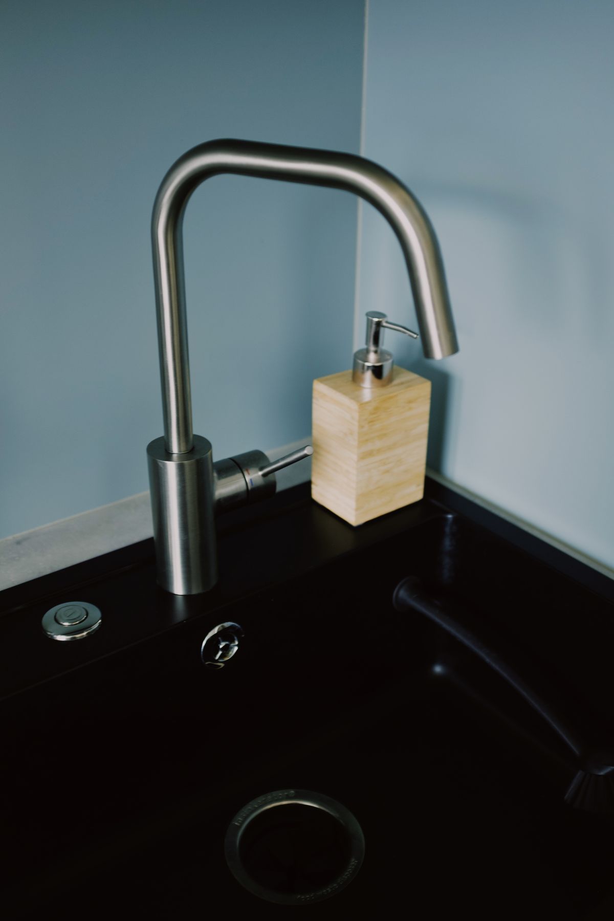 Stainless steel kitchen faucet and soap dispenser mounted on a dark sink deck