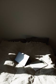 A serene bedroom setting with a laptop and book illuminated by natural sunlight.
