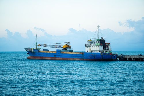 Free A large cargo ship moored at a pier, set against a tranquil blue ocean and sky backdrop. Stock Photo