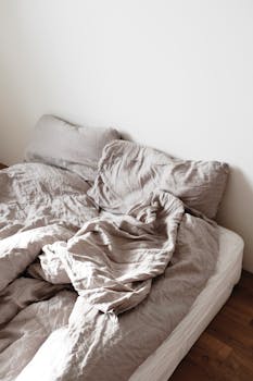 A cozy unmade bed with soft linen bedding in a minimalist bedroom setting, adding warmth and comfort.