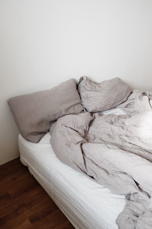 Unmade bed with pillows and blanket in light bedroom