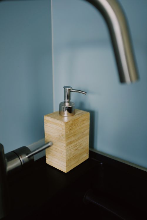 Free Close-up of a sleek stainless steel faucet and wooden soap dispenser in a modern kitchen setting. Stock Photo