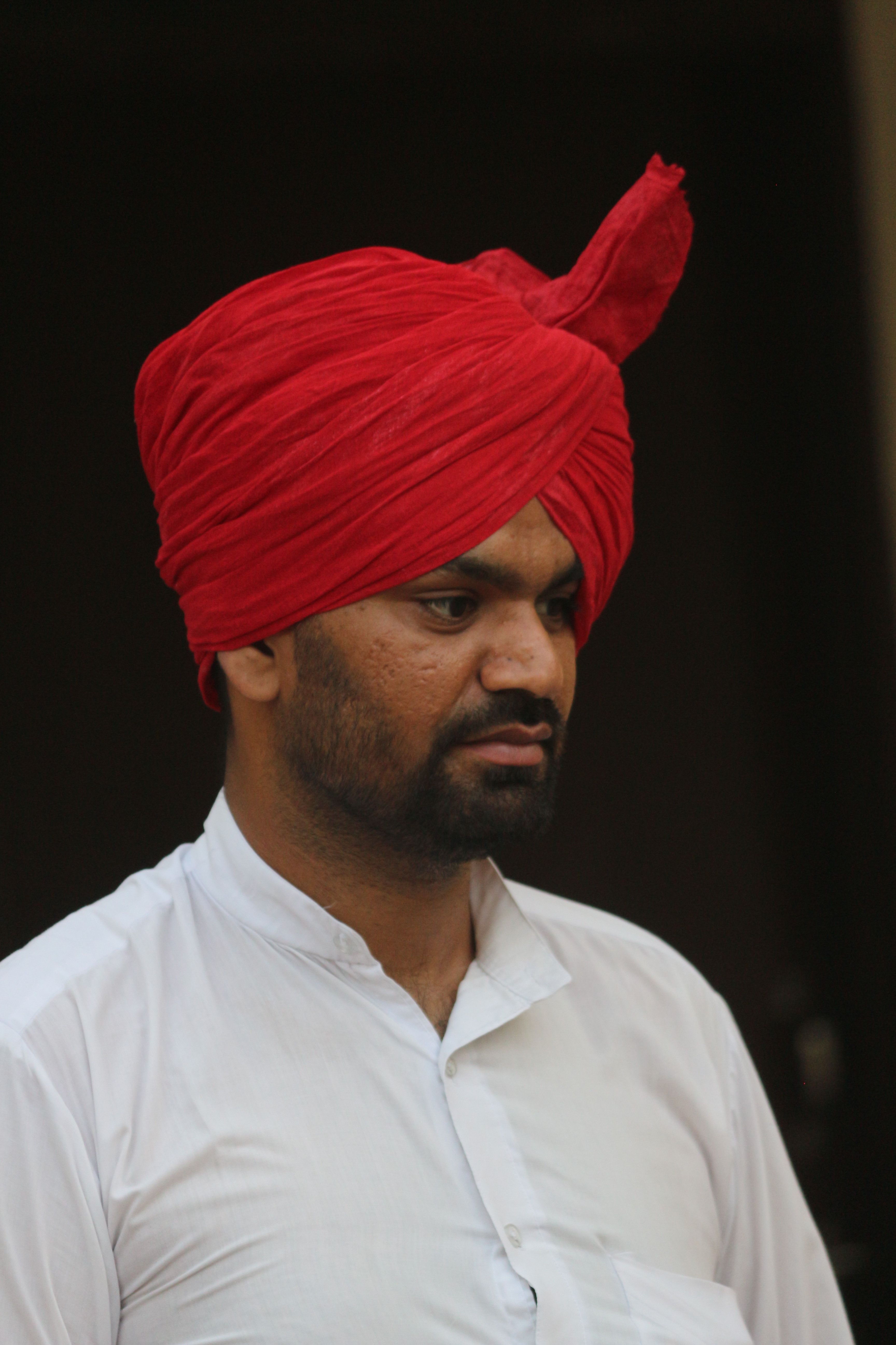 Man in red turban and white shirt, showcasing cultural attire with a serious expression.